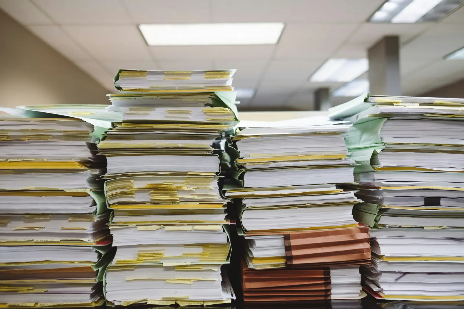 Pile di fascicoli e cartelle di documenti cartacei su una scrivania in ufficio