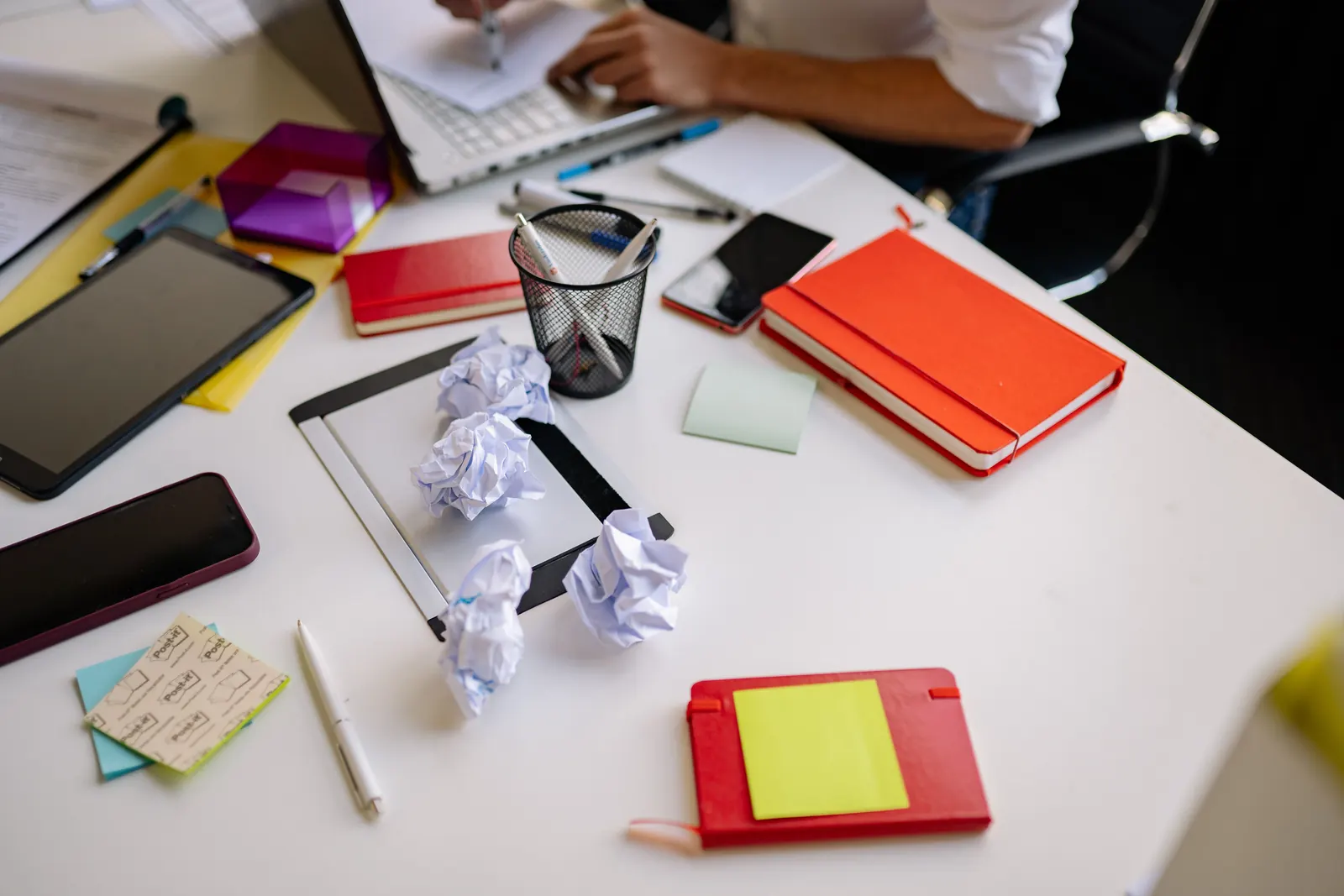 Scrivania d'ufficio disordinata con fogli accartocciati, quaderni colorati, post-it e un tablet
