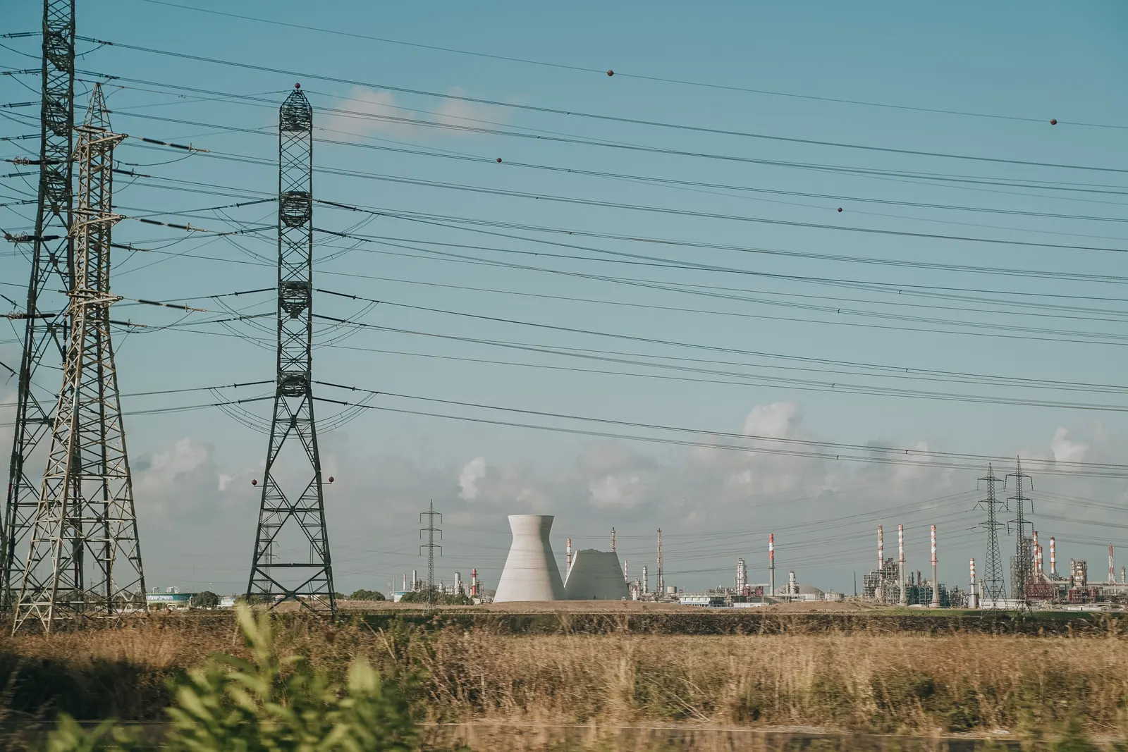 Tralicci dell'alta tensione e cavi elettrici sopra un prato secco con una centrale sullo sfondo