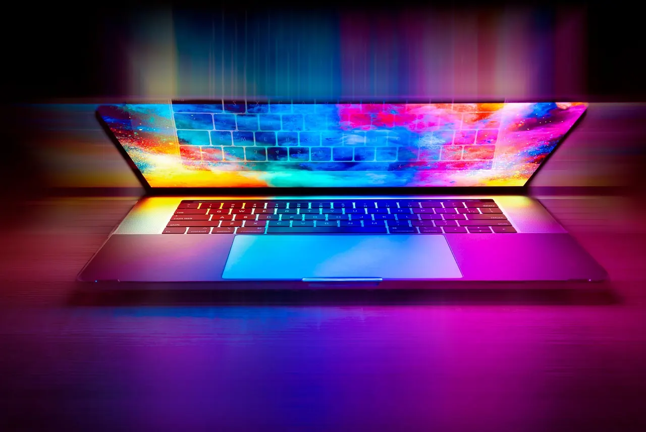 Laptop aperto con schermo e tastiera illuminati da luci colorate su sfondo scuro