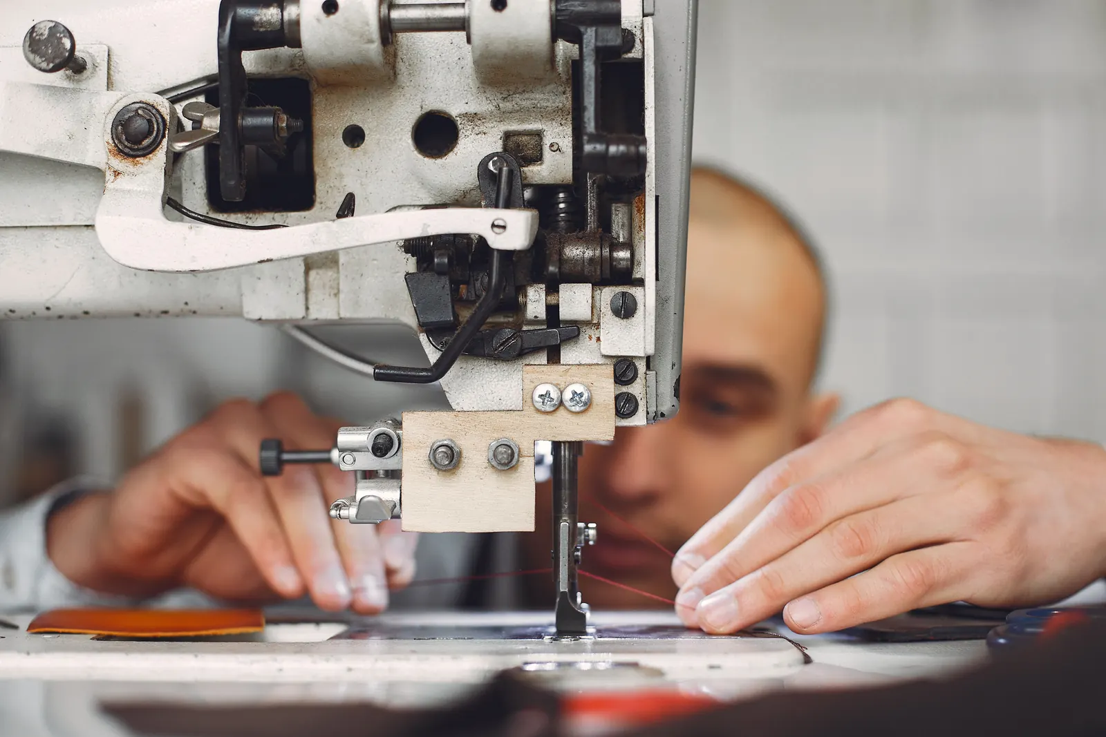 Mani di un artigiano che cuce un pezzo di pelle con una macchina da cucire industriale