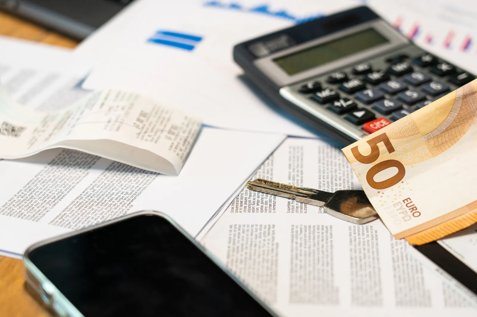 Calcolatrice, banconota da 50 euro, scontrino e fogli con grafici su una scrivania