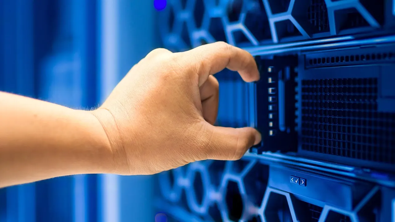 Mano che estrae un server da un armadio rack illuminato di blu in una sala server