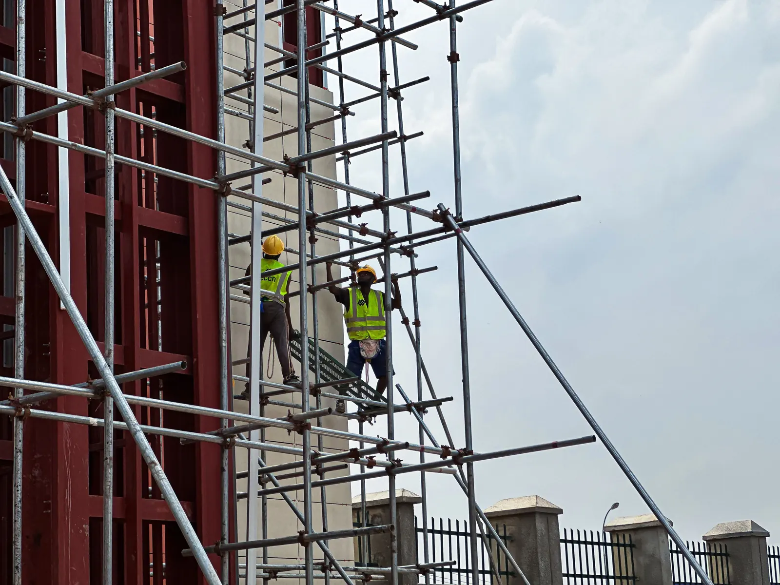 Due operai con casco giallo e gilet ad alta visibilità al lavoro su un ponteggio di un cantiere