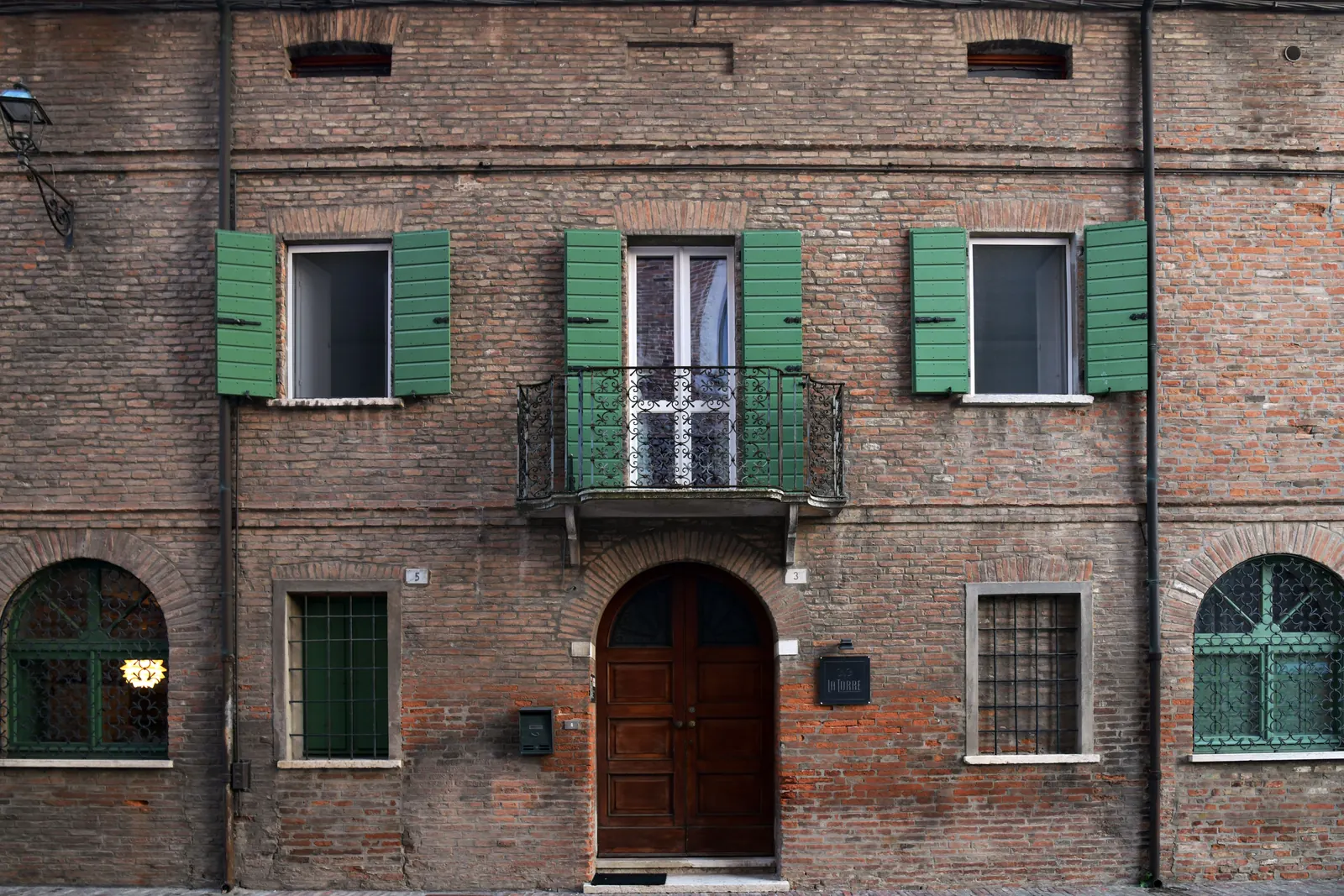 Facciata di un edificio in mattoni con persiane verdi, un balcone e portoni ad arco