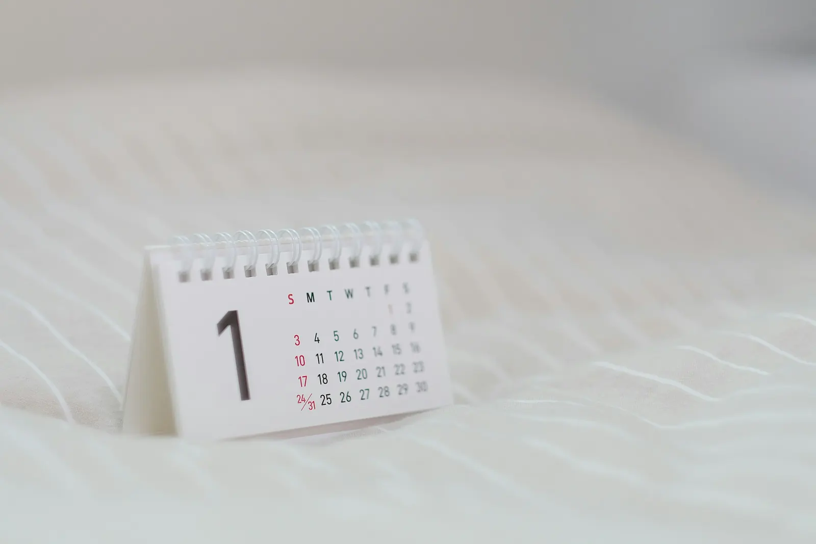 Calendario bianco con pagine a spirale appoggiato su un tessuto chiaro